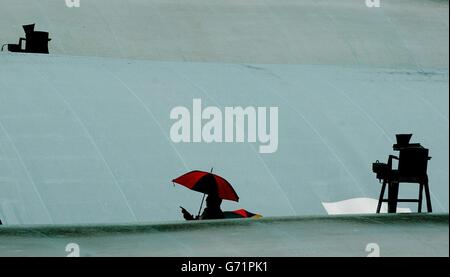 Tennisfans decken sich bei den Lawn Tennis Championships in Wimbledon, London, unter Regenschirmen, wo Regen und Stürme den Spielbeginn verzögerten. Stockfoto