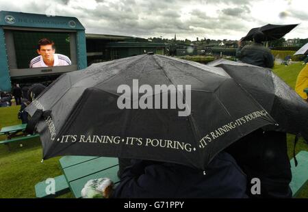 Tennisfans decken sich unter Regenschirmen, während sie sich heute bei den Lawn Tennis Championships in Wimbledon, London, auf der Großleinwand Wiederholungen von Spielen ansehen, bei denen Regen und Stürme den Spielbeginn verzögerten. 24/06/04: Spieler und Zuschauer in Wimbledon beteten für gutes Wetter in der Hoffnung, dass heftiger Regen nicht einen weiteren Tag Tennis zerstören würde. Erst zum achten Mal in den letzten 30 Jahren war der dritte Spieltag bei den diesjährigen Meisterschaften eine komplette Auswaschung, da anhaltende Regengüsse und starker Wind SW19 trafen. Stockfoto