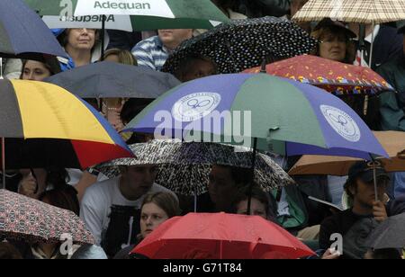 Tennis-Fans schützen sich vor dem Regen auf dem Center Court bei den Lawn Tennis Championships in Wimbledon. Der Spielbeginn wurde wegen der Duschen verzögert. KEIN HANDY Stockfoto
