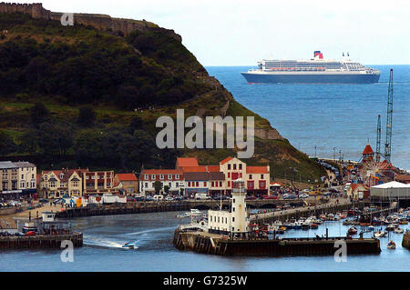 Die Klippen um Scarborough Bay, North Yorkshire, sind die Spitze, wenn das größte Passagierflugzeug der Welt, Queen Mary 2, vorbeifährt. Stockfoto