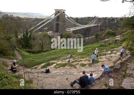 Kinder gleiten auf einer natürlichen Felsrutsche in der Nähe der Clifton Suspension Bridge, die von Isambard Kingdom Brunel entworfen wurde und die die Avon Gorge und den Fluss Avon überspannt und Clifton in Bristol mit Leigh Woods in North Somerset verbindet. Die Brücke wurde 1864 eröffnet und ist ein denkmalgeschütztes Gebäude der Klasse I, das Teil der Straße B3129 ist, für die eine Maut zu überqueren ist Stockfoto