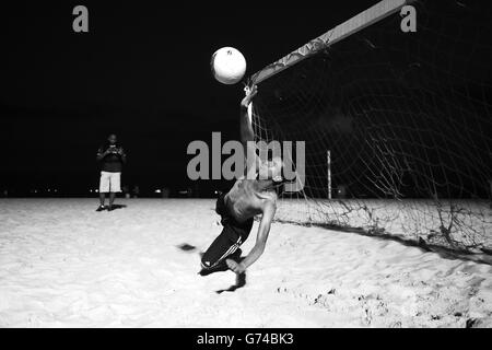 Ein brasilianischer Junge spielt Fußball unter Flutlicht am Strand von Coabba in Rio de Janeiro Stockfoto