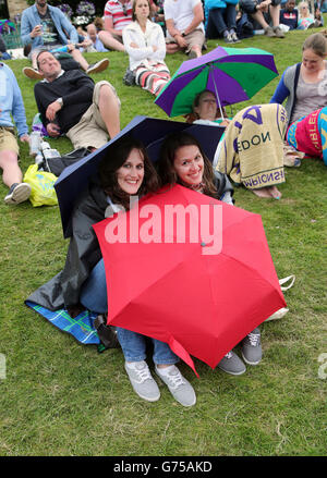 Die Fans fangen an, sich unter Regenschirmen zu bedecken, wenn es am vierten Tag der Wimbledon Championships beim All England Lawn Tennis and Croquet Club in Wimbledon regnet. Stockfoto