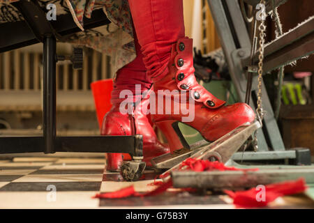 Rote Stiefel der Näherin am Fußanlasser für Nähmaschine Stockfoto