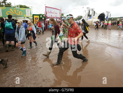 Festivalbesucher gehen beim Glastonbury Festival auf der Worthy Farm in Somerset vorsichtig durch eine Schlammpfütze. Stockfoto