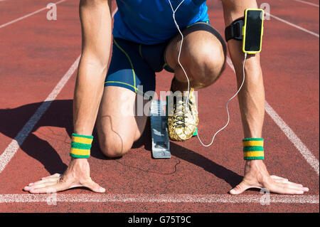 Sportler an der Startlinie eine Laufstrecke von seinem Mobiltelefon zu motivierender Musik über Kopfhörer hören hocken Stockfoto