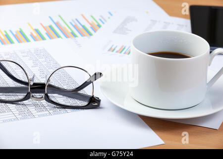 Tasse schwarzen Kaffee und ein paar Brillen Handauflegen eines Buchhalters Schreibtisch auf einer Tabellenkalkulation und einige Grafiken Stockfoto