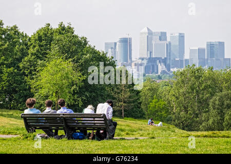 Junge Leute sitzen auf einer Bank im Greenwich Park, Blick auf das Canary Wharf Banking Bezirk Skyline, London Stockfoto