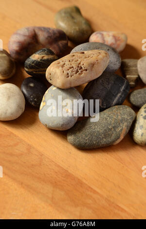 Felsen in verschiedenen Formen und Farben auf hellen Holztisch liegen. Maserung des Holzes ist auf der Diagonalen. Kopieren Sie Platz unten. Stockfoto