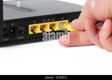 Hand ein gelbes Netzwerkkabel an einen Netzwerk-Port des Routers anschließen Stockfoto