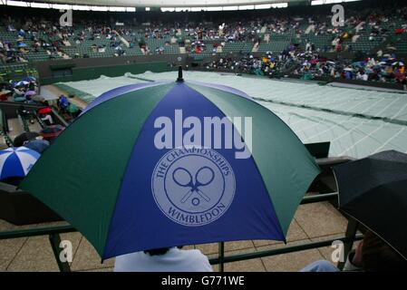 FÜR , KEINE KOMMERZIELLE VERWENDUNG. Tennis-Fans schützen sich vor dem Regen auf Court One während des Spiels zwischen Richard Krajicek aus den Niederlanden und Mark Philippoussis aus Australien in Wimbledon. Stockfoto
