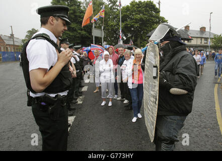 Ein loyalistischer Unterstützer, der als Polizeibeamter für Krawalle gekleidet ist, nähert sich der Polizei, während sie auf eine Parade des Orangenen Ordens in der Crumlin Road warten, die an das nationalistische Ardoyne-Viertel anschließt, als Teil der jährlichen Feierlichkeiten zum zwölften Juli. Markiert den Sieg von König Wilhelm III Sieg über James II in der Schlacht von Boyne in 1690. Stockfoto