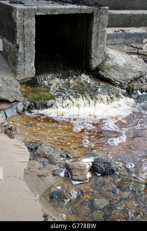 Regenwasser fließt aus einem Gully am Strand Stockfoto