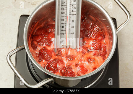 Thermometer messen die Temperatur der Erdbeermarmelade in einer Pfanne Kochen Stockfoto
