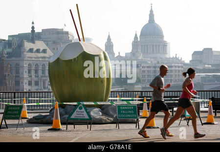 Jogger kommen an einer riesigen Kokosnuss vorbei, die von Vita Coco auf der Londoner South Bank platziert wurde, um die Londoner daran zu erinnern, während der Hitzewelle hydratisiert zu bleiben. Stockfoto