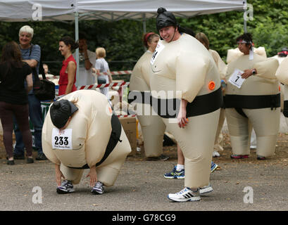 Die Teilnehmer wärmen sich vor der Teilnahme am Sumo Run - einem 5 km langen Charity-Lauf für Läufer in aufblasbaren Sumo-Anzügen - im Battersea Park, London auf. Stockfoto