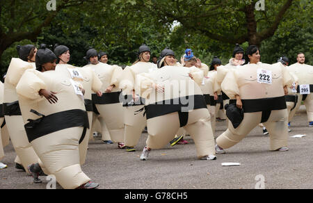 Die Teilnehmer wärmen sich vor der Teilnahme am Sumo Run - einem 5 km langen Charity-Lauf für Läufer in aufblasbaren Sumo-Anzügen - im Battersea Park, London auf. Stockfoto