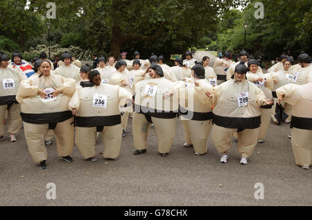 Die Teilnehmer wärmen sich vor der Teilnahme am Sumo Run - einem 5 km langen Charity-Lauf für Läufer in aufblasbaren Sumo-Anzügen - im Battersea Park, London auf. Stockfoto