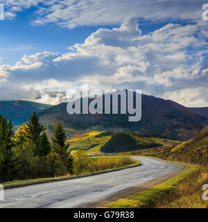 Asphaltstraße geht in den Berg hinein führt durch den grünen schattigen Wald in der Nähe von ländlichen Orten Stockfoto