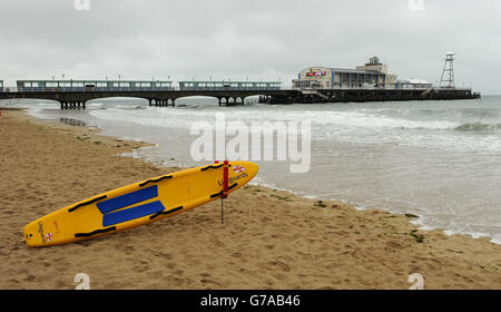 RNLI Rettungsschwimmer Bestand. Ein RNLI Lifeguard Surfbrett liegt am Strand von Bournemouth im Schatten des Piers Stockfoto
