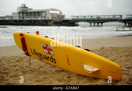 Am Strand liegt ein RNLI Rettungsschwimmer Surfbrett Bournemouth im Schatten des Piers Stockfoto