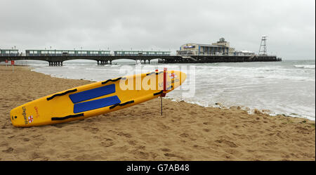 Am Strand liegt ein RNLI Rettungsschwimmer Surfbrett Bournemouth im Schatten des Piers Stockfoto