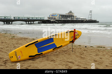 RNLI Rettungsschwimmer Bestand. Ein RNLI Lifeguard Surfbrett liegt am Strand von Bournemouth im Schatten des Piers Stockfoto