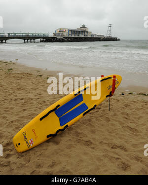 Am Strand liegt ein RNLI Rettungsschwimmer Surfbrett Bournemouth im Schatten des Piers Stockfoto