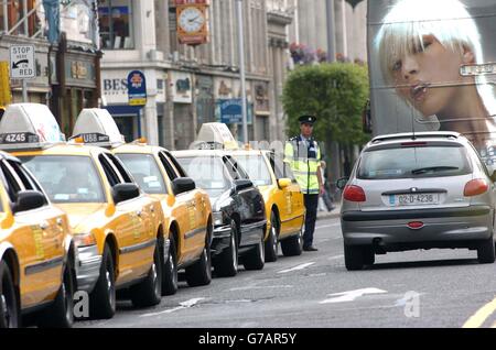 Ein Garda hält den Verkehr im Auge, der an geparkten gelben Taxis im US-Stil vorbeifährt, und zwar an der Filmkulisse einer Nachstellung von "The Honeymooners" in der O'Connell Street, Dublin, Irland. Hunderte von Menschen versammelten sich, um zu beobachten, wie die Gegend von Set-Bauherren und Requisiten verwandelt wurde, um wie eine typische Straße in den USA auszusehen. Stockfoto