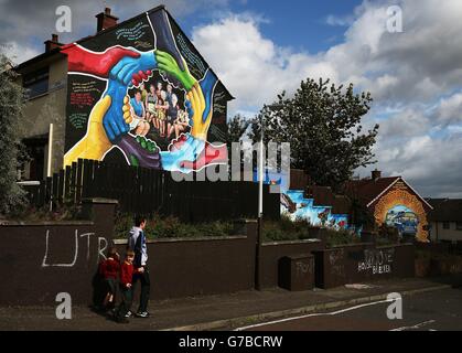 Caolan Cahill, 15, sein Bruder Ruairi und seine Zwillingsschwester Aoibhin, sechs, machen sich auf den Weg von der Schule, vorbei an einem Wandgemälde, das an der Seite eines Hauses im Anwesen Ballymurphy in Belfast gemalt wurde. Stockfoto