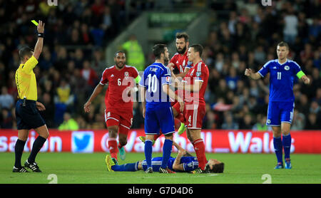 Wales' James Chester (rechts) und Bosnien und Herzegowinas Miralem Pjanic (links) treffen aufeinander, während der Schiedsrichter Vladislav Bezborodov während des UEFA Euro 2016-Spiels im Cardiff City Stadium, Cardiff, eine gelbe Karte schwingt. Stockfoto