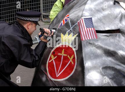 Ein Polizeibeamter filmt Demonstranten von Trident Plowshares, von denen einige an ein großes U-Boot vor den Toren der Downing Street 10 im Zentrum von London angekettet wurden. Die Gesichter der Demonstranten - mit dem gelben und schwarzen dreiblättrigen Strahlungswarnsymbol bemalt - strichen aus einigen der vielen Bullaugen des U-Bootes hervor, während sie an ihren Handgelenken im Inneren des U-Bootes angekettet saßen. Stockfoto