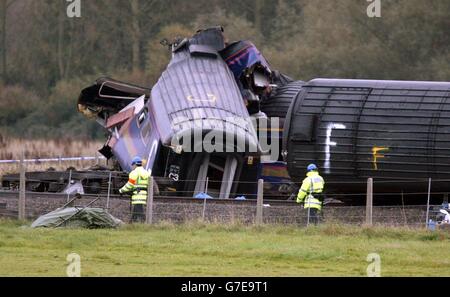 Beamte gehen an dem Zug vorbei, der am Samstag auf einem abgelegenen Bahnübergang in der Nähe von Ufton Nervet in Berkshire mit einem Limousine fuhr. Sechs Menschen starben bei dem Einschlag und ein Siebter starb am Sonntag im Krankenhaus. Die Polizei, die den Vorfall untersucht, konzentriert sich darauf, warum ein Autofahrer sein Auto in den Weg des Zuges geparkt hat. Alle Leichen wurden nun von der Baustelle entfernt und ein Kran wird gebaut, um das Wrack zu räumen. 06/12/2004 die Multi-Millionen-Pfund-Rechnung für den Crash, der sieben Menschen getötet und Dutzende verletzt, wird aus einem Cash-Pot von der Versicherungsbranche von Fahrern finanziert bezahlt werden Stockfoto