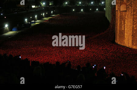 Die Öffentlichkeit hält an, um sich die Keramikmohn anzusehen, die Teil der Kunstinstallation „Blood Swept Lands and Seas of Red“ des Künstlers Paul Cummins im Tower of London sind und den hundertsten Jahrestag des Ersten Weltkriegs feiern. Stockfoto