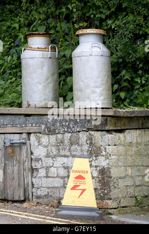 alte Milchkannen auf eine Mauer mit einer Warnung zu unterzeichnen "Gefahr Freileitungen" Stockfoto