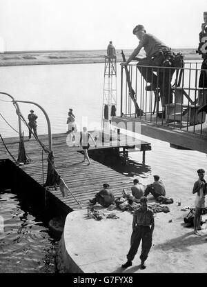 Ein bewaffneter Wachposten wacht von oben, wenn britische Soldaten der anglo-französischen Streitkräfte vom Anlegesteg der Suez Company im Suezkanal baden. Stockfoto