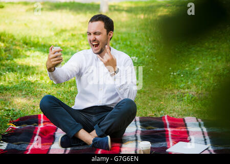 Foto von hübscher netter Kerl im Freien am Morgen. Junger Mann lächelnd und Selfie Foto auf Handy mit coolen ausdrücken Stockfoto