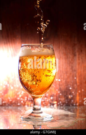 Bier fließt, Glas mit Tropfen auf dunklem Hintergrund Stockfoto