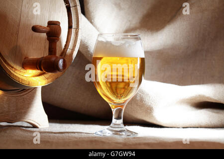 Glas voll Bier mit Schaum in der Nähe von Holzfass Stockfoto