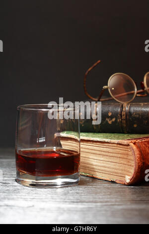 Stillleben mit Glas Whiskey in der Nähe von alte Bücher auf dunklem Hintergrund Stockfoto