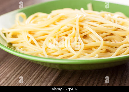 Gekochte Spaghetti schlicht in eine grüne Platte auf einem Holztisch serviert Stockfoto