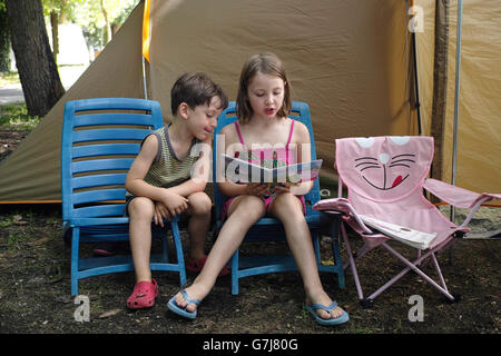 Lago di Bracciano. Lazio Rom. Italien. Sechs Jahre altes Mädchen lesen zu einem Jünger 4 Jahre alten Jungen auf Campingurlaub. Stockfoto