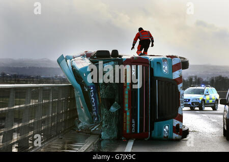 Ein Lastwagen liegt auf seiner Seite, nachdem er bei starkem Wind auf der Clackmannanshire Bridge über den Firth of Forth, Schottland, überwehen wurde, da starke Winde einen weiteren Tag der Störung der britischen Verkehrsnetze gebracht haben, während Warnungen vor heftigen Böen bestehen bleiben, Schnee und Eis über den Großteil des Wochenendes. Stockfoto