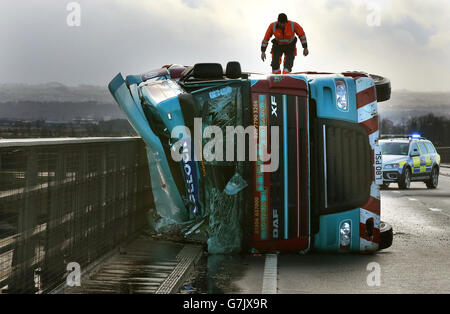 Ein Mann klettert auf einem Lastwagen auf seiner Seite, nachdem er bei starkem Wind auf der Clackmannanshire Bridge über den Firth of Forth, Schottland, hinübergeweht wurde, da starke Winde einen weiteren Tag der Störung der britischen Verkehrsnetze gebracht haben, während Warnungen für heftige Böen bestehen bleiben, Schnee und Eis über den Großteil des Wochenendes. Stockfoto