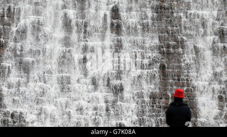 Eine Frau blickt auf den Derwent-Damm im Peak District, der nach dem kürzlichen starken Regen und starken Wind überfließt. Stockfoto