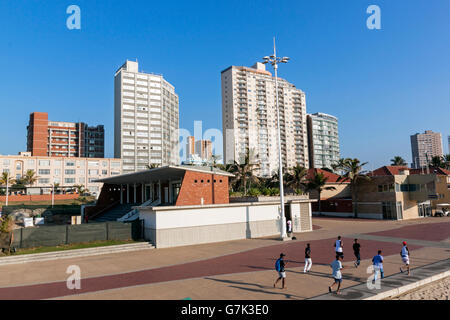 Sieben Morgen Jogger am Strand gepflasterte Promenade gegen Skyline der Stadt Stockfoto