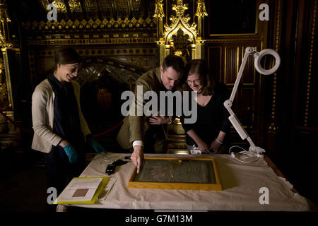 Die Salisbury Cathedral 1215 Kopie der Magna Carta wird von (von links nach rechts) Parlamentarischer Archivkonservatorin Oriana Calman, Chris Woods, dem Direktor des National Conservation Service und Salisbury Cathedral Archivarin Emily Naish, Bevor er in einem Kabinett aufgestellt wurde, das neben den anderen drei erhaltenen OriginalPergamentfesseln der Magna Carta anlässlich des 800. Jahrestages der Versiegelung von Magna Carta in Runnymede im Jahr 1215 im Robing Room der Queen im Houses of Parliament in London ausgestellt werden soll. Stockfoto