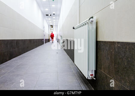 Weiße Heizkörper in langen, schmalen Korridor mit gelockerten Wand und Boden. Stockfoto