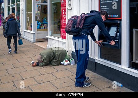 Ein junger Mann mit Geldautomaten auf Princes Street, Edinburgh, während eine junge Frau in der Nähe bittet. Stockfoto