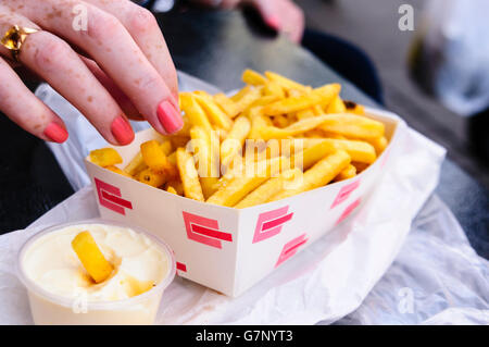 Eine Frau nimmt ein Braten aus einer Schachtel Pommes frites neben einer Wanne mit Mayonnaise. Stockfoto
